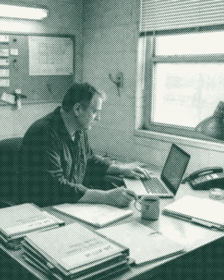 A workshop owner at his office desk with a laptop and job folders